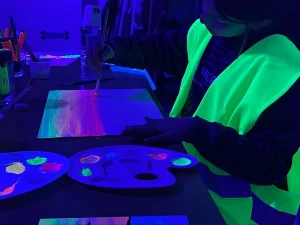 Imagen de una niña que se sumerge en un mundo de colores vibrantes. La habitación está bañada en una luz suave y encantadora, donde la magia de los neones transforma una actividad ordinaria en un espectáculo extraordinario. Correspondiente a la categoría de tallesres creativos. -Sitios para celebrar fiestas con niños en Barcelona